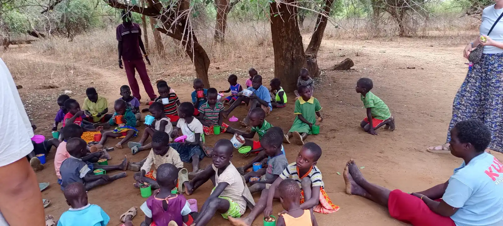 Children sitting in the shade with cups of food